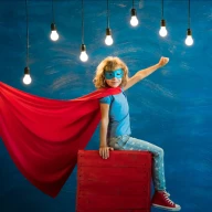 Dziecko ubrane na niebiesko z maską z czerwoną peleryną